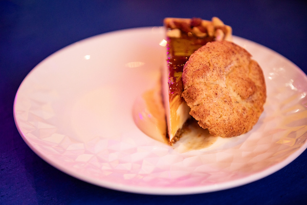 A slice of pie on a white glass plate, with a cookie leaned against it.